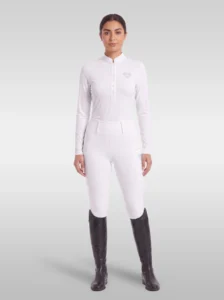 Rider wearing the white Elite Competition long sleeve base layer with white breeches and tall riding boots, full body