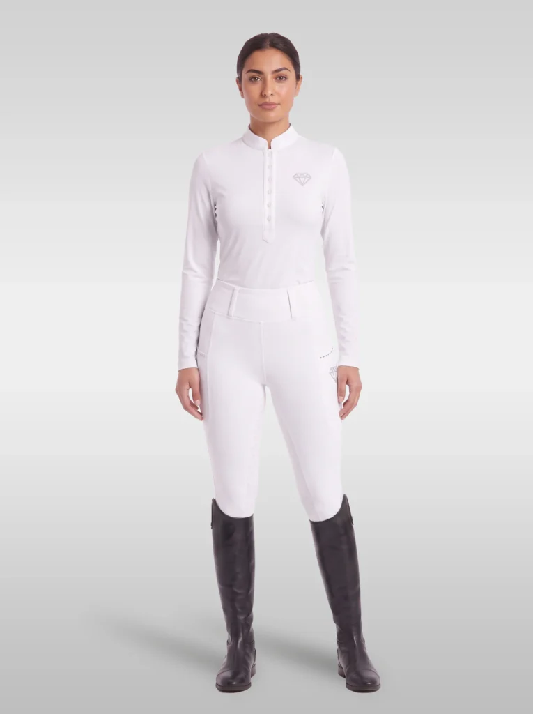 Rider wearing the white Elite Competition long sleeve base layer with white breeches and tall riding boots, full body