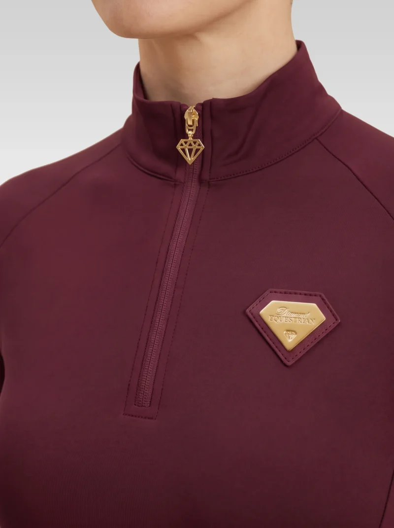 Close-up of the burgundy Prestige base layer: gold zip with diamond pull and gold metal Diamont Equestrian badge in a burgundy leather frame