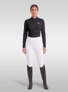 Rider wearing the black Elite Competition long sleeve base layer with white breeches and tall riding boots, full body