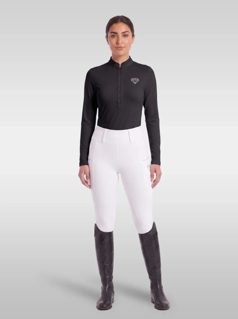 Rider wearing the black Elite Competition long sleeve base layer with white breeches and tall riding boots, full body