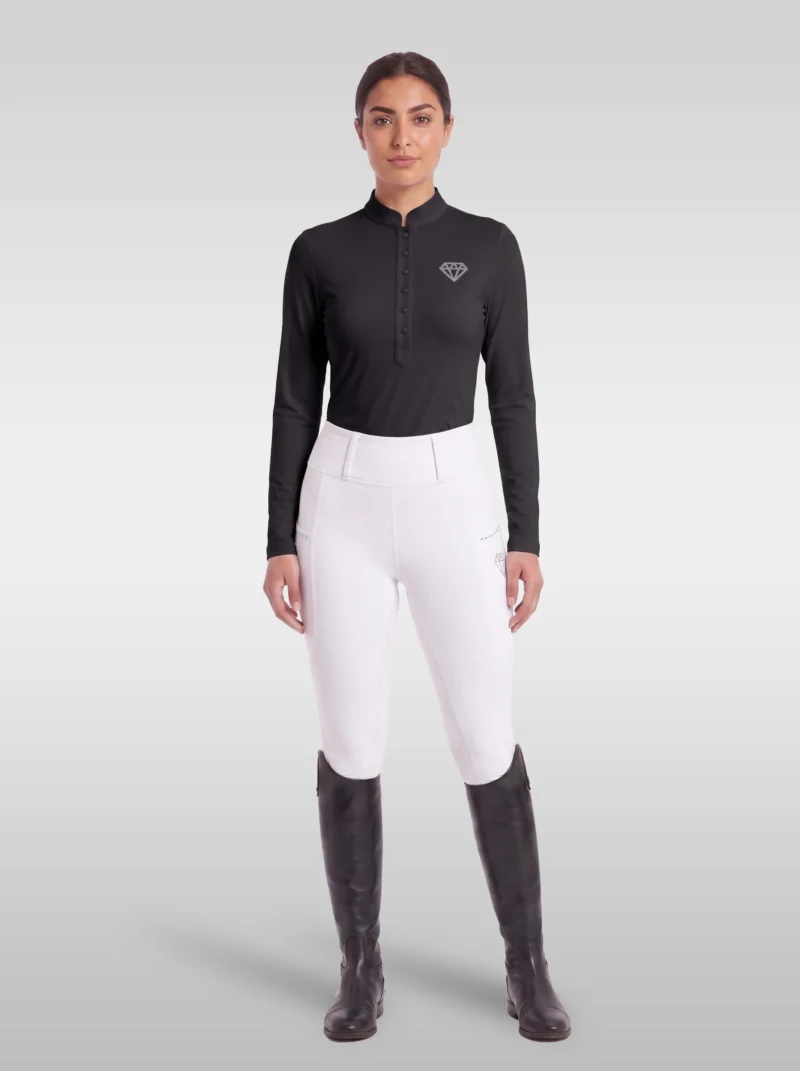 Rider wearing the black Elite Competition long sleeve base layer with white breeches and tall riding boots, full body
