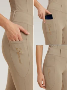 Close-up details of beige riding leggings: side phone pocket holding a smartphone and Diamont script