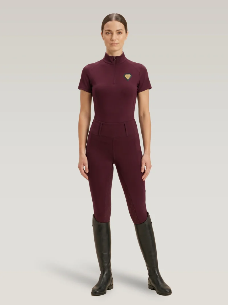 Rider wearing burgundy Prestige riding leggings with a matching Diamont Equestrian base layer and tall riding boots, full body