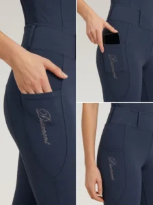 Close-up details of navy riding leggings: side phone pocket holding a smartphone and Diamont script