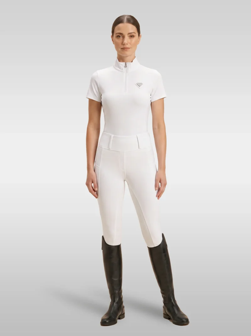 Rider wearing the white Prestige base layer with white riding breeches and tall riding boots, full body