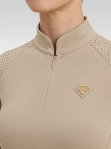 Close-up of the beige Prestige long sleeve base layer: Diamont signature on the collar, quarter-zip, perforated shoulder panel and gold metal badge