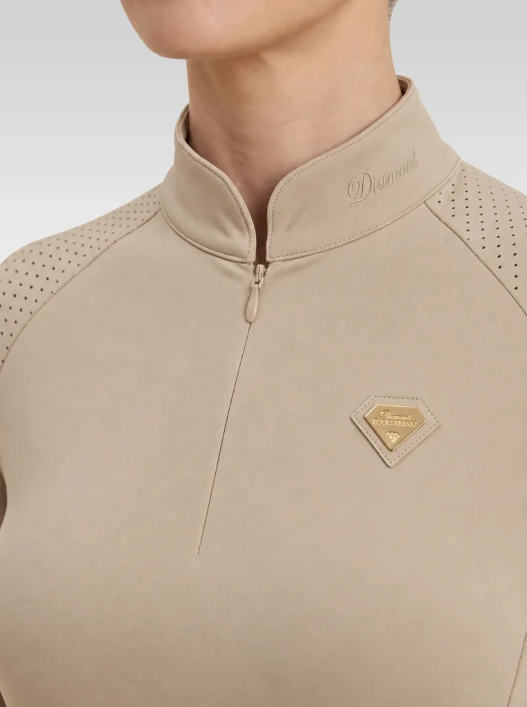 Close-up of the beige Prestige long sleeve base layer: Diamont signature on the collar, quarter-zip, perforated shoulder panel and gold metal badge