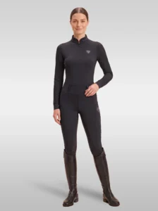Rider wearing the black Prestige long sleeve base layer with matching black riding leggings and tall riding boots, full body