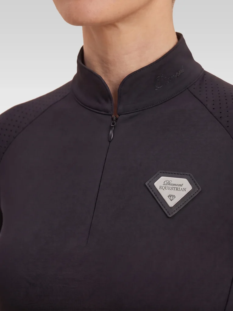Close-up of the black Prestige long sleeve base layer: stand-up collar, quarter-zip, perforated shoulder panel and silver metal badge in a black leather frame