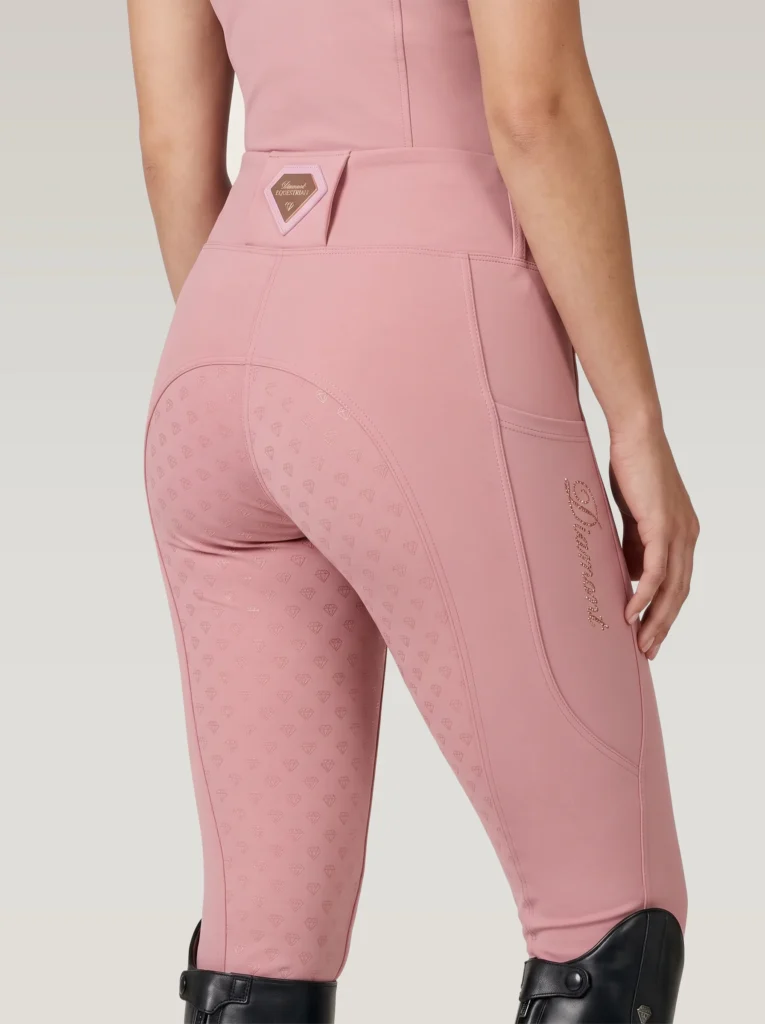 Back three-quarter view of blush pink equestrian leggings with full-seat diamond grip, waistband badge and Diamont script