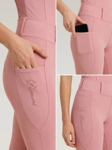 Close-up details of blush pink riding leggings: side phone pocket holding a smartphone and Diamont script