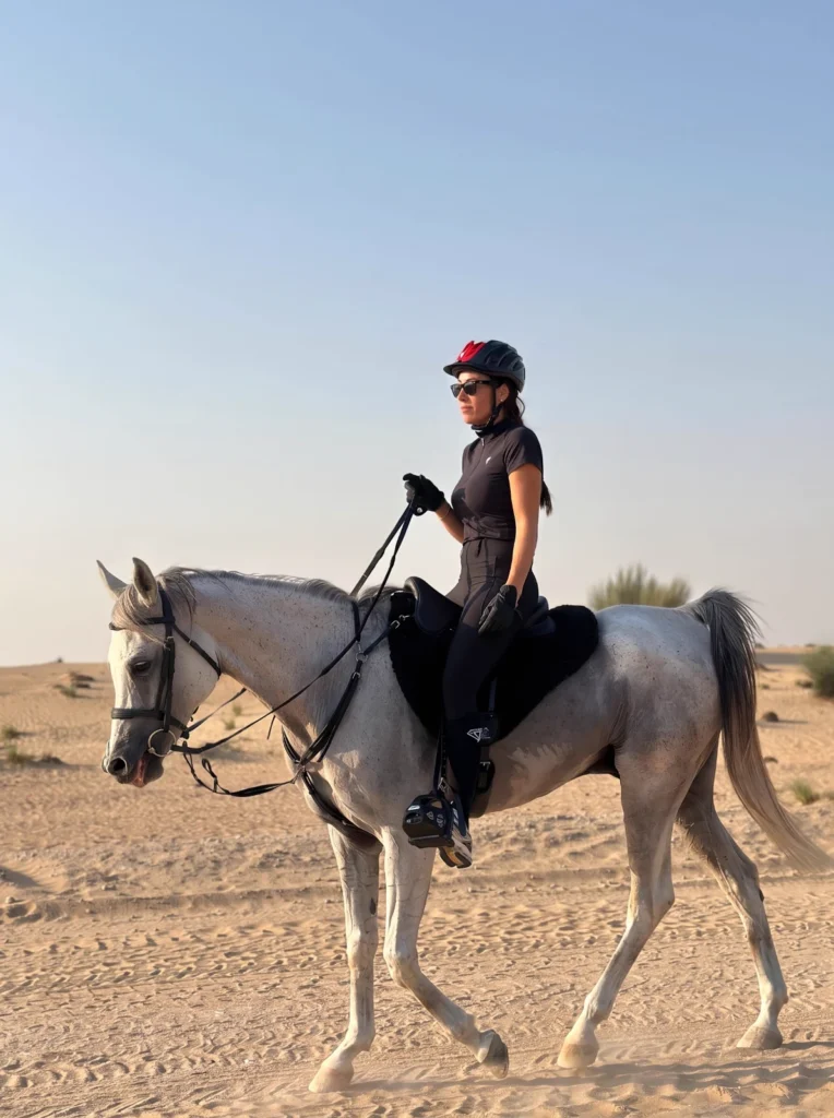 Nanda, owner of Diamont Equestrian, riding a grey horse in the Dubai desert in black Diamont riding wear