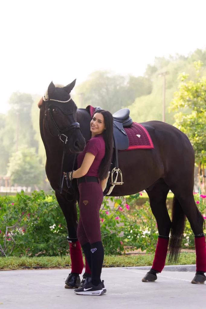 Dressage rider Sinah with her horse Sandokan in Diamont Equestrian burgundy riding leggings, base layer and matching saddle pad