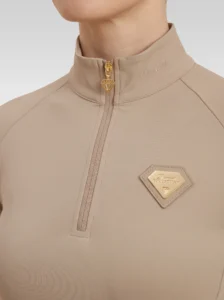 Close-up of the beige Prestige base layer: gold zip with diamond pull and gold metal Diamont Equestrian badge in a beige leather frame