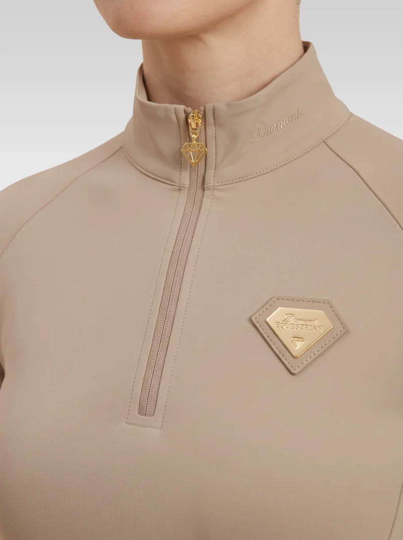 Close-up of the beige Prestige base layer: gold zip with diamond pull and gold metal Diamont Equestrian badge in a beige leather frame