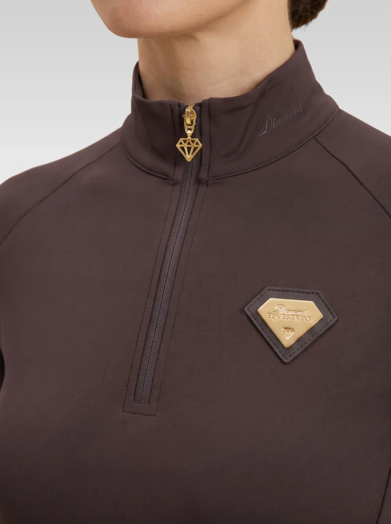 Close-up of the chocolate Prestige base layer: gold zip with diamond pull and gold metal Diamont Equestrian badge in a brown leather frame