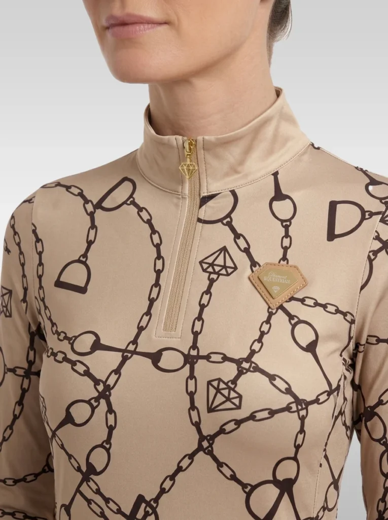 Close-up of the beige Signature long sleeve base layer: stand-up collar, gold quarter-zip, chain and stirrup print and gold metal diamond badge